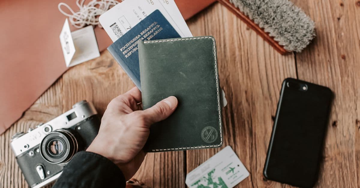 Mano sosteniendo un pasaporte con funda sobre una mesa con pase de abordar, cámara y celular listos para viajar