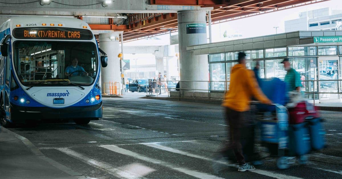 Belebtes Flughafenterminal mit wartenden Reisenden und einem Bus unter überdachtem Abholbereich
