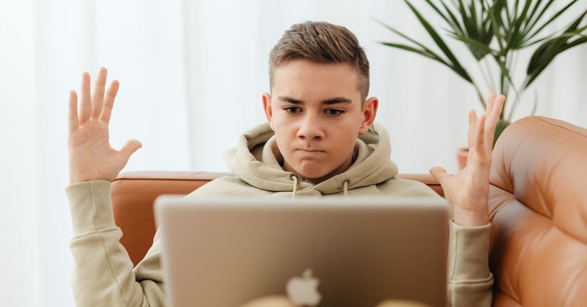 Tiener kijkt gefrustreerd naar laptop op de bank terwijl hij een KPN storing probeert te melden.