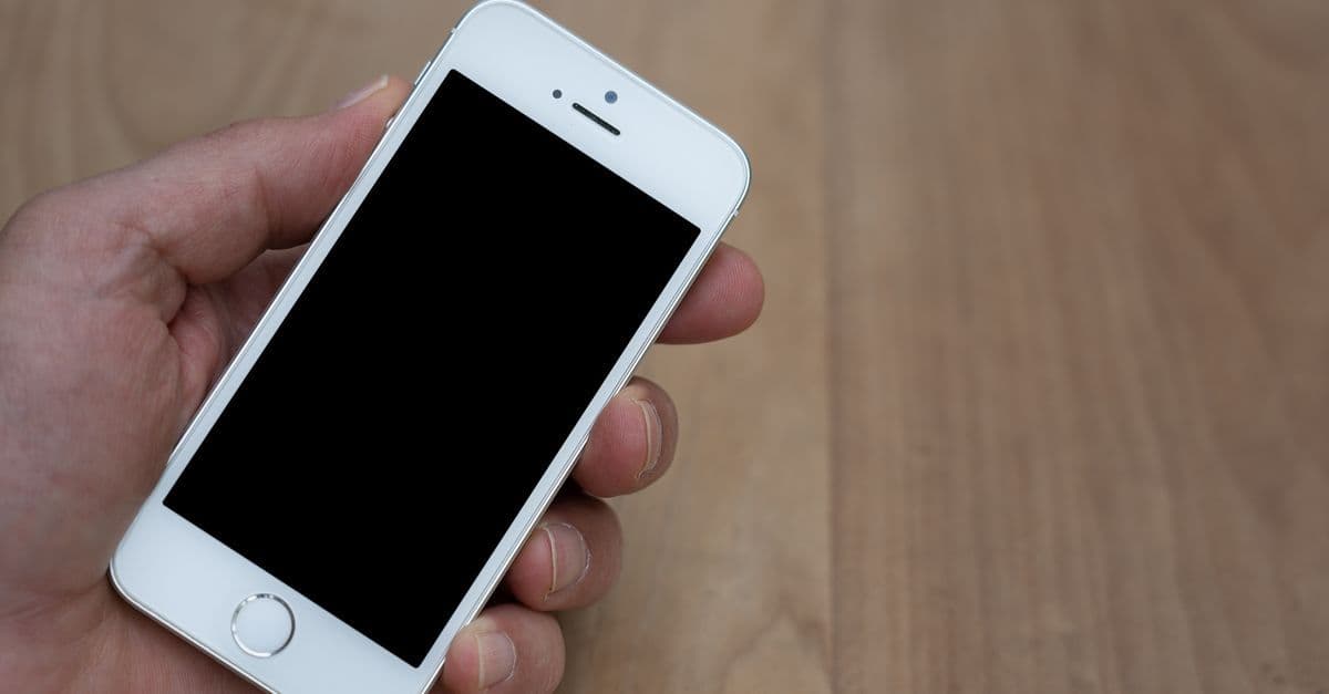 iphone 初期化が失敗し画面が表示されないスマートフォンを木製テーブルの上で手に持つ様子