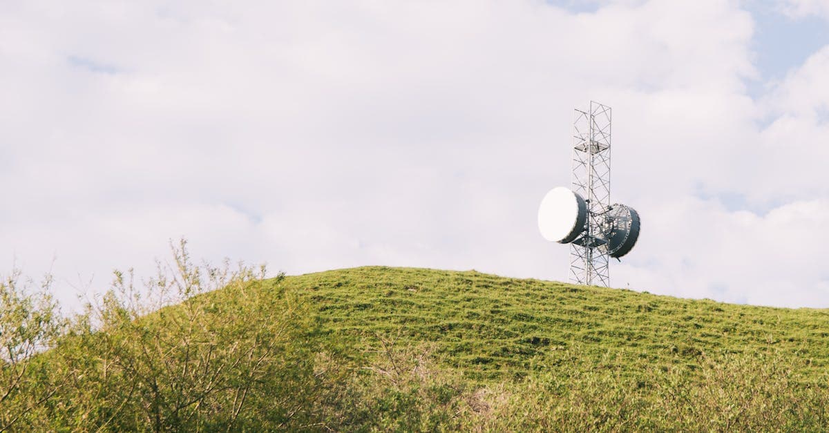 Mobile communication tower on a grassy hill under a cloudy sky, representing UK broadband network coverage.