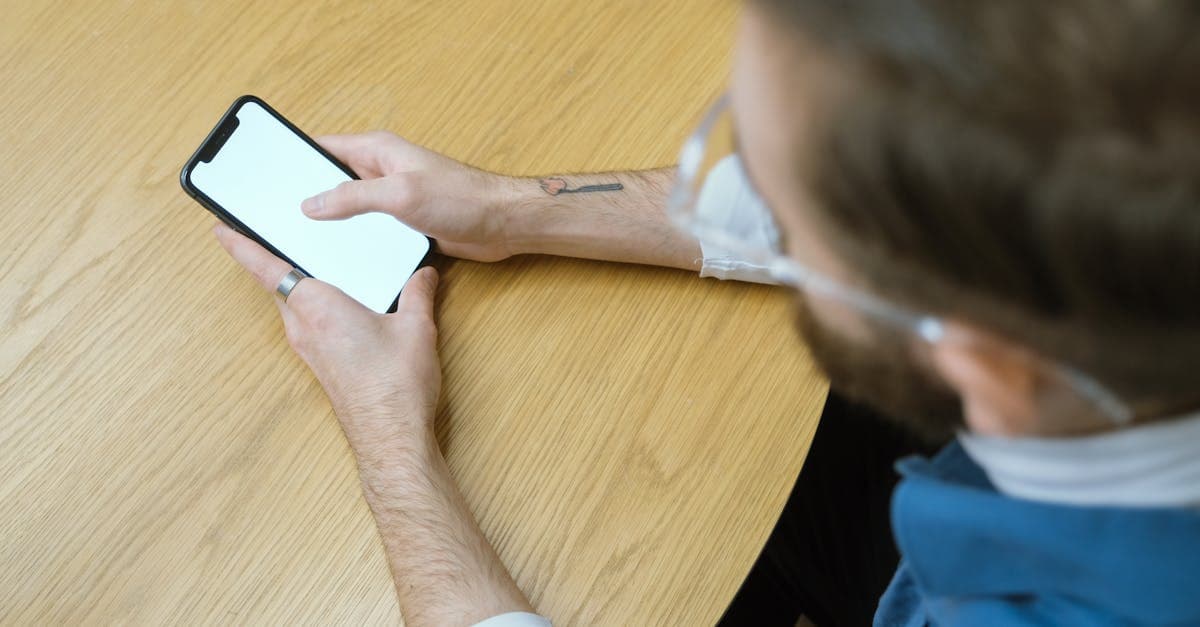 木製テーブルで空白スクリーンのスマートフォンを持つ人物の俯瞰。dアカウント確認方法に関するよくある質問をまとめた場面。