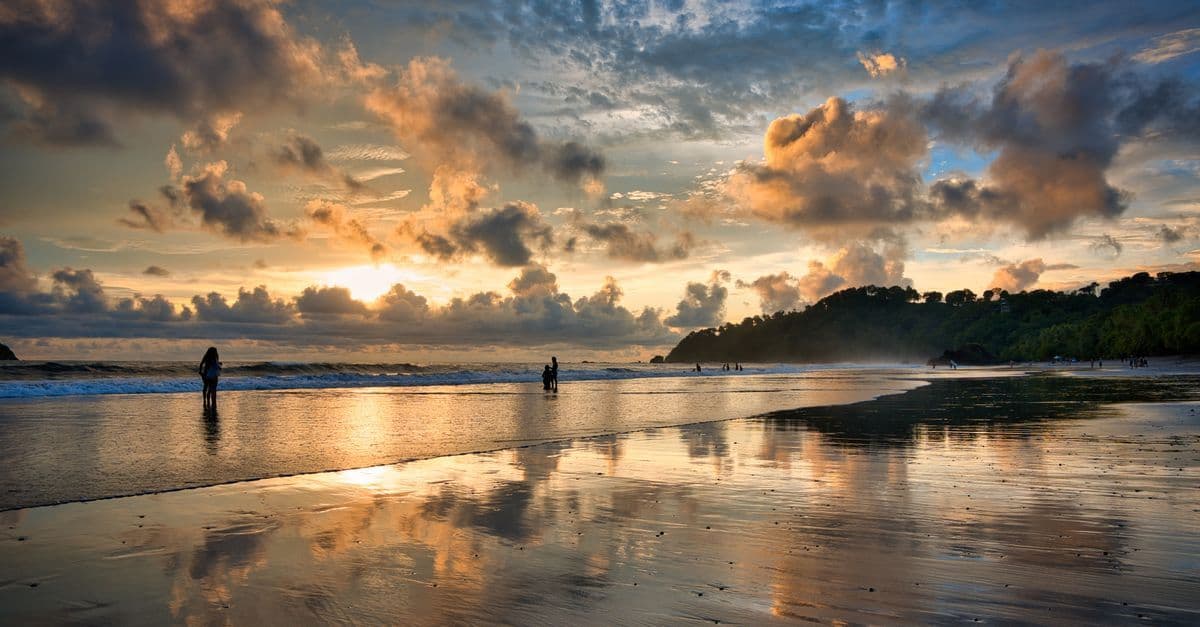 Deux personnes se tiennent dans l’eau sur une plage tropicale au coucher du soleil.