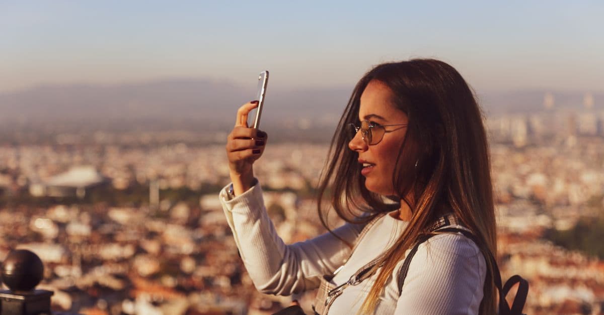 Young woman taking a selfie at sunset in Barcelona, using a travel eSIM to stay connected abroad.