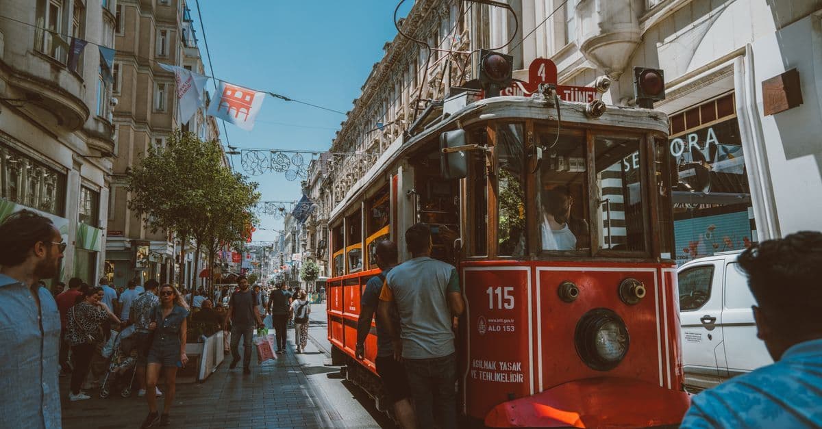 A red tram carries passengers along a busy Istanbul street lined with shops and historic buildings.