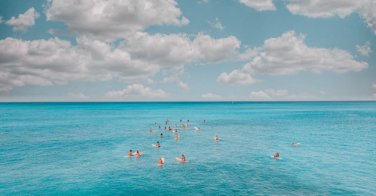 Bagnanti nuotano in un mare turchese sotto un cielo azzurro punteggiato di nuvole.