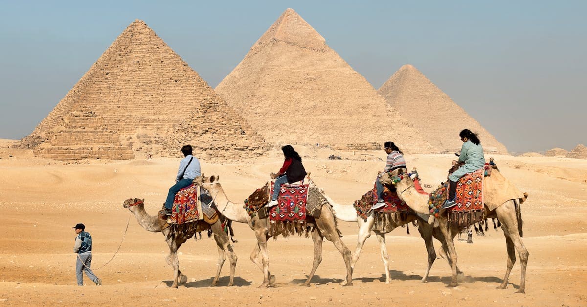 Turister rider på kameler foran de store pyramider i Giza under klar blå himmel