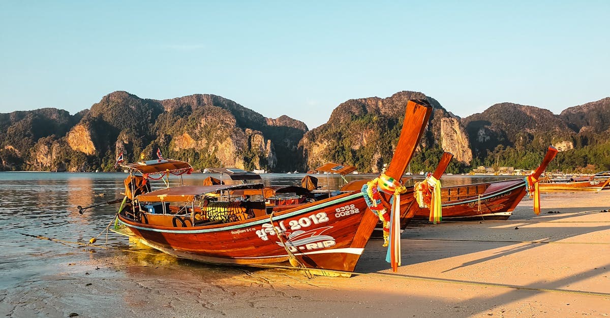 Bunte Longtail-Boote an einem stillen Thai-Strand bei Sonnenuntergang vor beeindruckenden Karstfelsen in Thailand