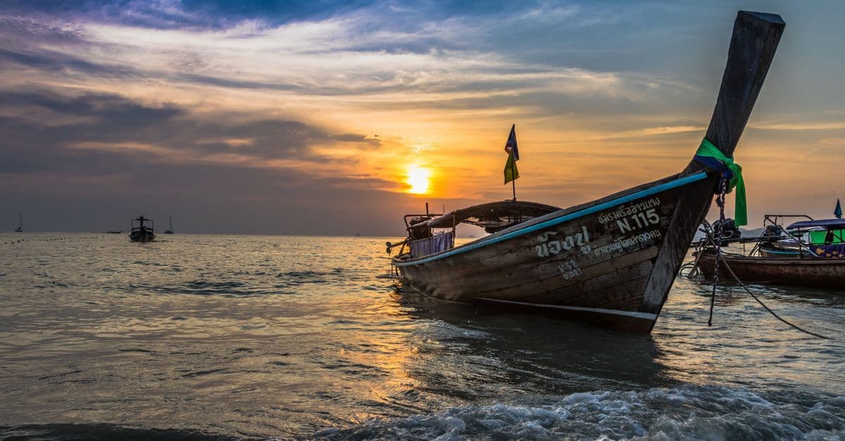 Golden sunset over a Thai beach with traditional fishing boats, perfect for planning holidays to Thailand.