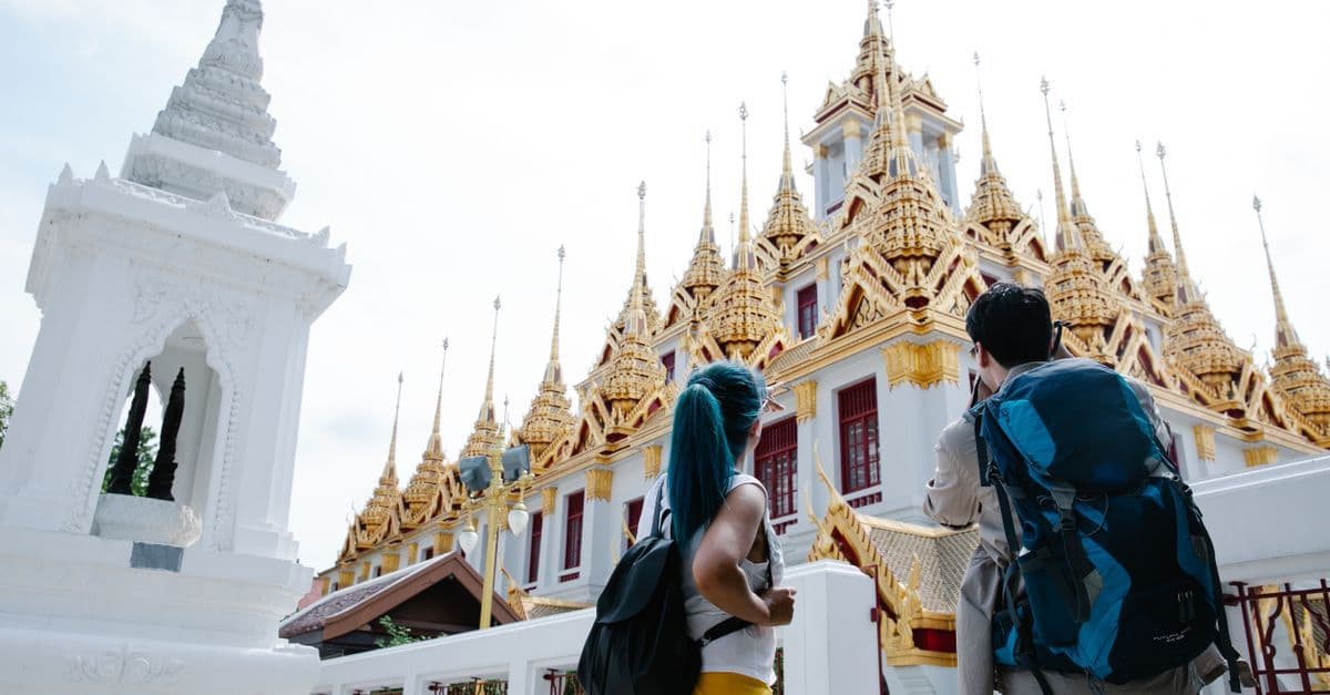 นักท่องเที่ยวสองคนสะพายเป้ชมความงามวัดไทยโบราณ กำลังหาประกันการเดินทางต่างประเทศที่ดีที่สุด