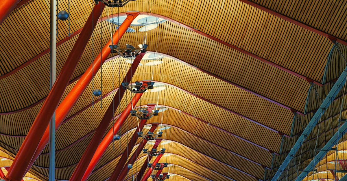Plafond géométrique emblématique de l'aéroport de Madrid-Barajas, avec ses arches et ses poteaux rouges.