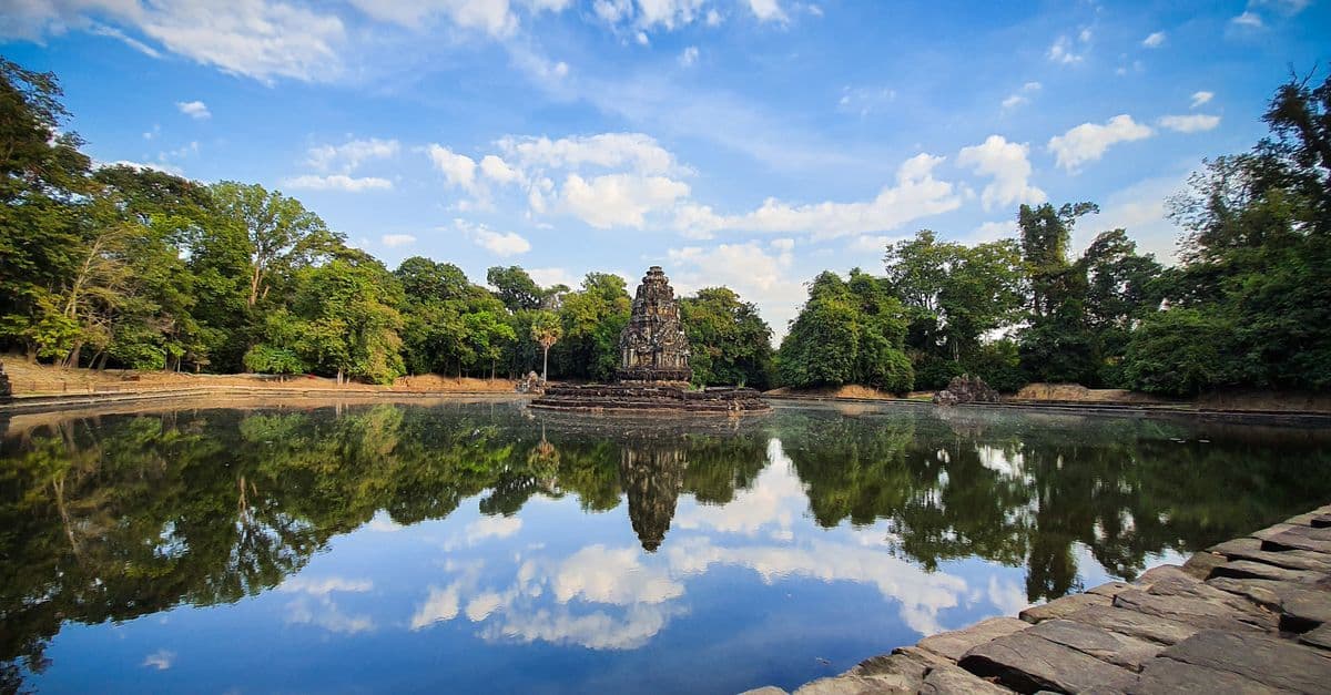 青空の下、森に囲まれた古代寺院が水面に美しく映る、海外旅行先の風景。
