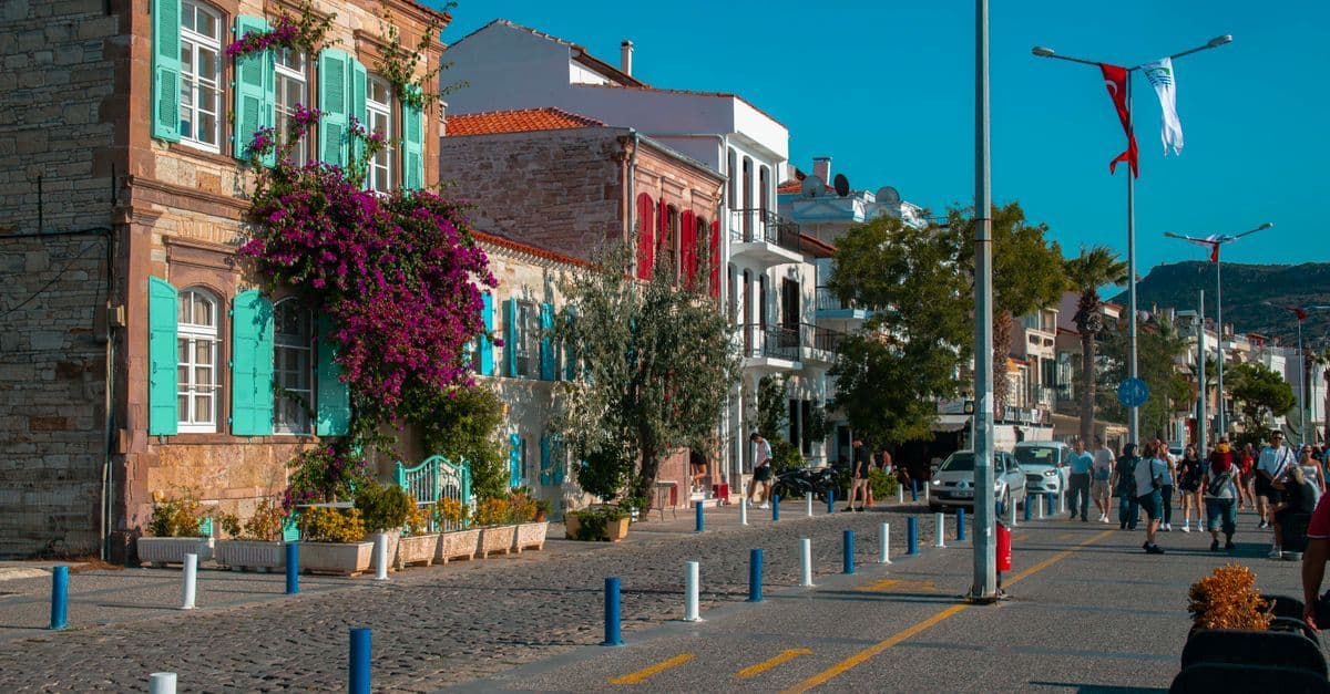 Nadmorska ulica w miasteczku Foça w Turcji: kamienice z turkusowymi okiennicami, sklepy i spacerowicze.