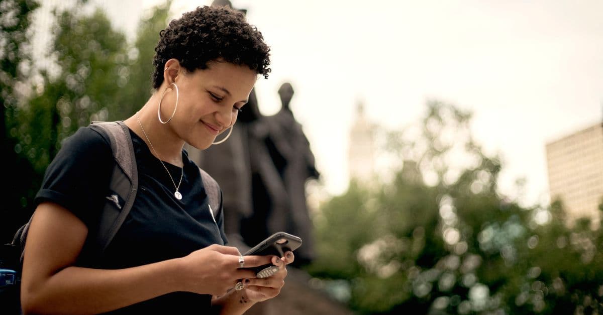 Smiling woman texting on her phone in a Chicago park while staying connected abroad