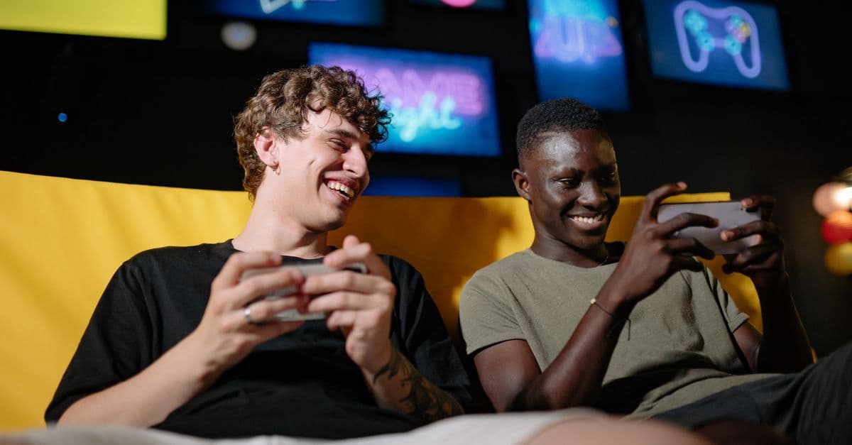 Two young men laughing and enjoying Gartic Phone game modes together on a mobile device.