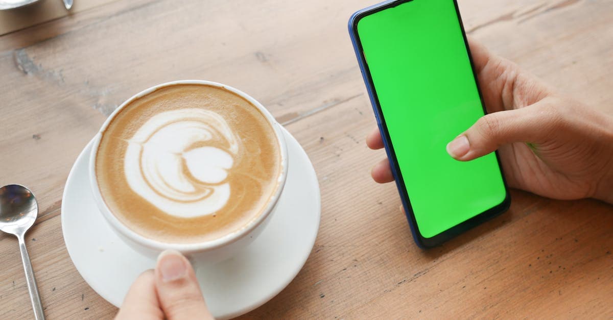 木製テーブルに置かれたラテとスマートフォンのクローズアップ。自分のdアカウントを調べる手順を確認しているシーン。