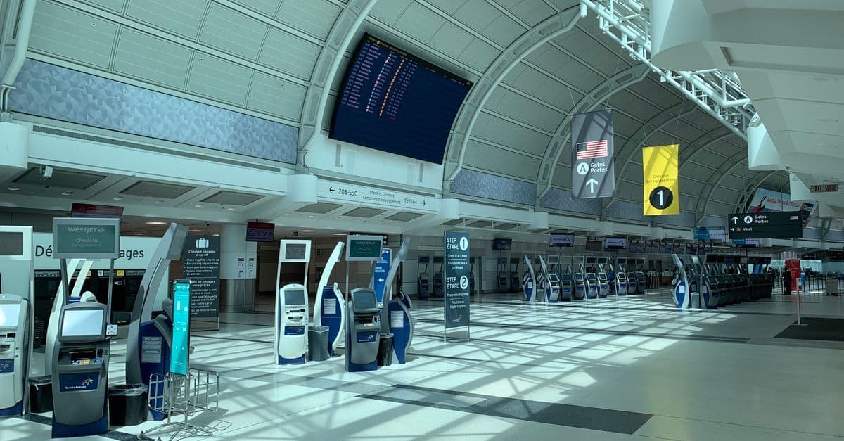 Interior moderno de un aeropuerto canadiense con corredor, tableros de información y señalización.