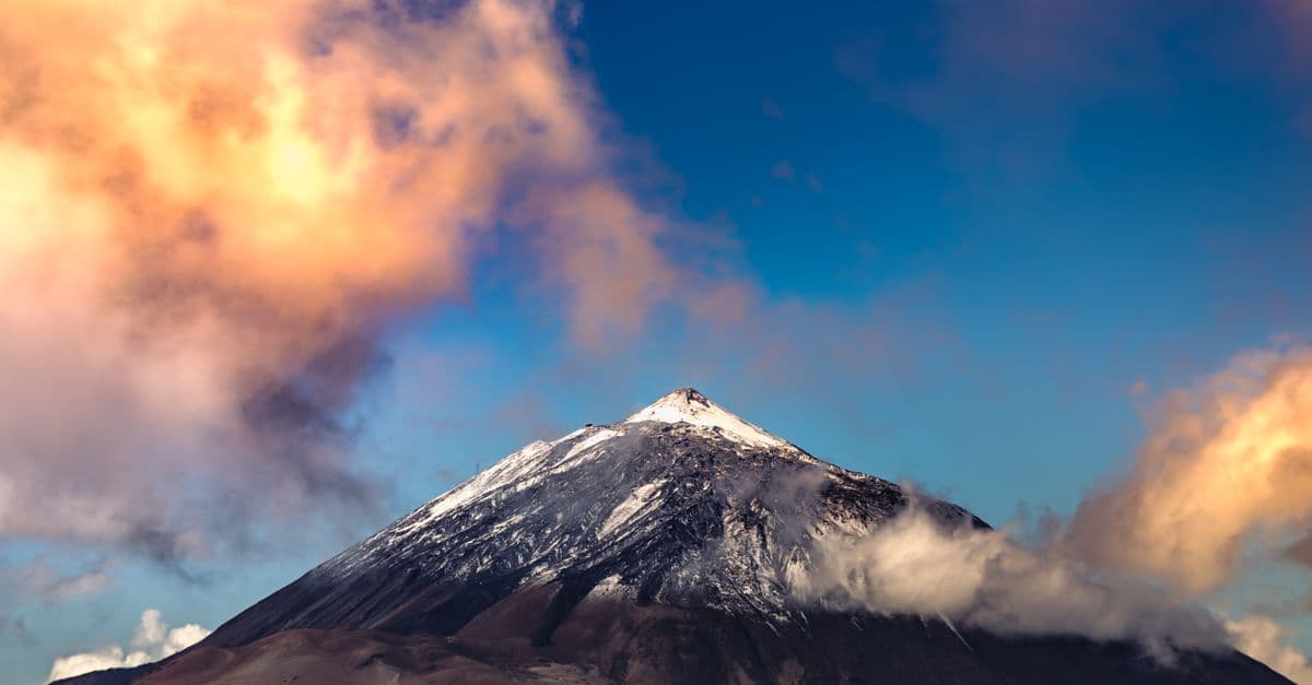 Mount Teide's snow-capped peak with clouds lit by the setting sun.