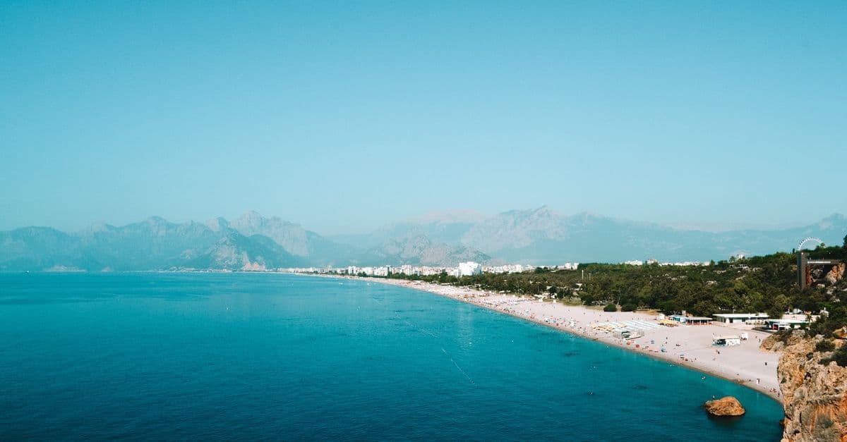 Blick von oben auf den Konyaaltı-Strand in Antalya mit türkisblauem Meer und Bergen im Hintergrund.