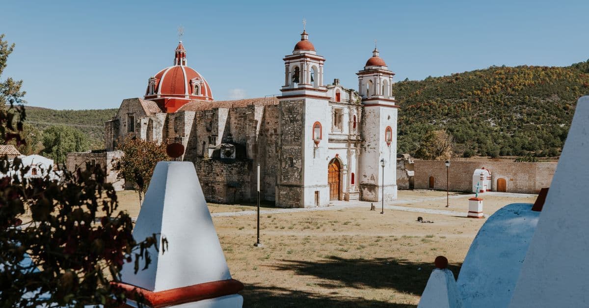 Historic rural church with distinctive red domes under clear blue skies near Oaxaca.