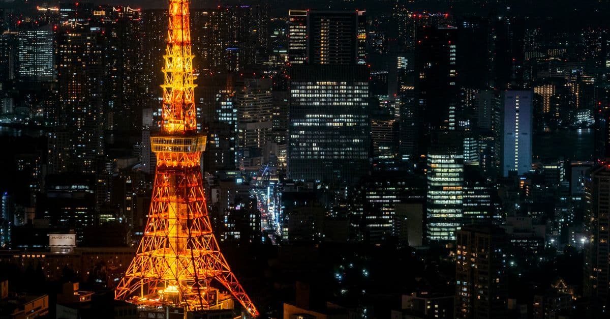 Tokyo Tower illuminata di notte con lo skyline della città sullo sfondo, simbolo della connettività metropolitana.