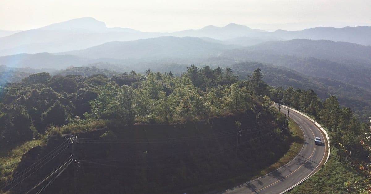 Haze softens rows of forested hills as a road curves around a mountainside in Chiang Mai, Thailand.