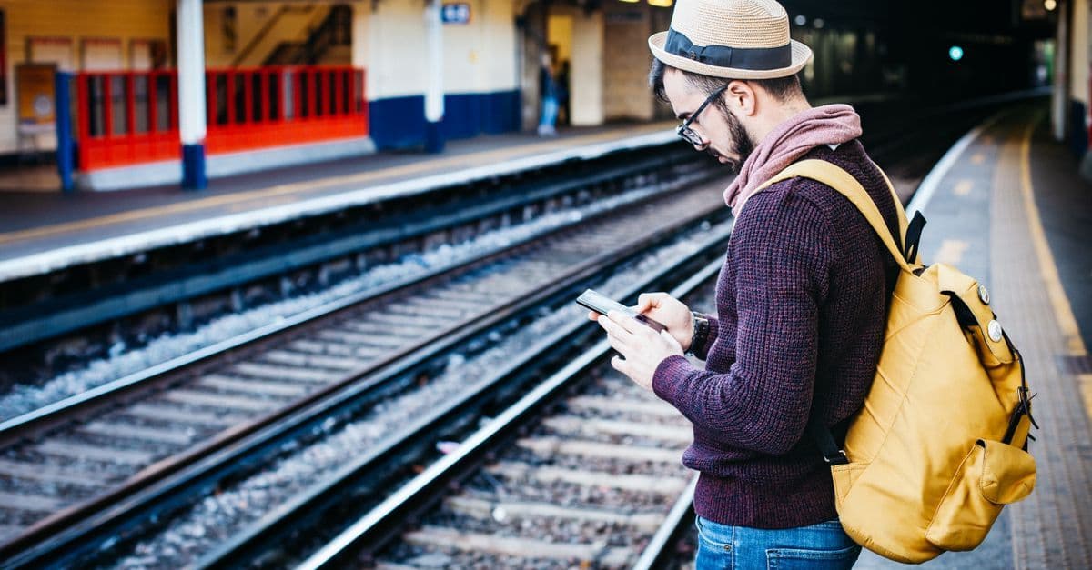 Spontanreisender mit Rucksack telefoniert am Stadtbahnhof – so bleibt man auf Last-Minute-Reisen im Ausland erreichbar.