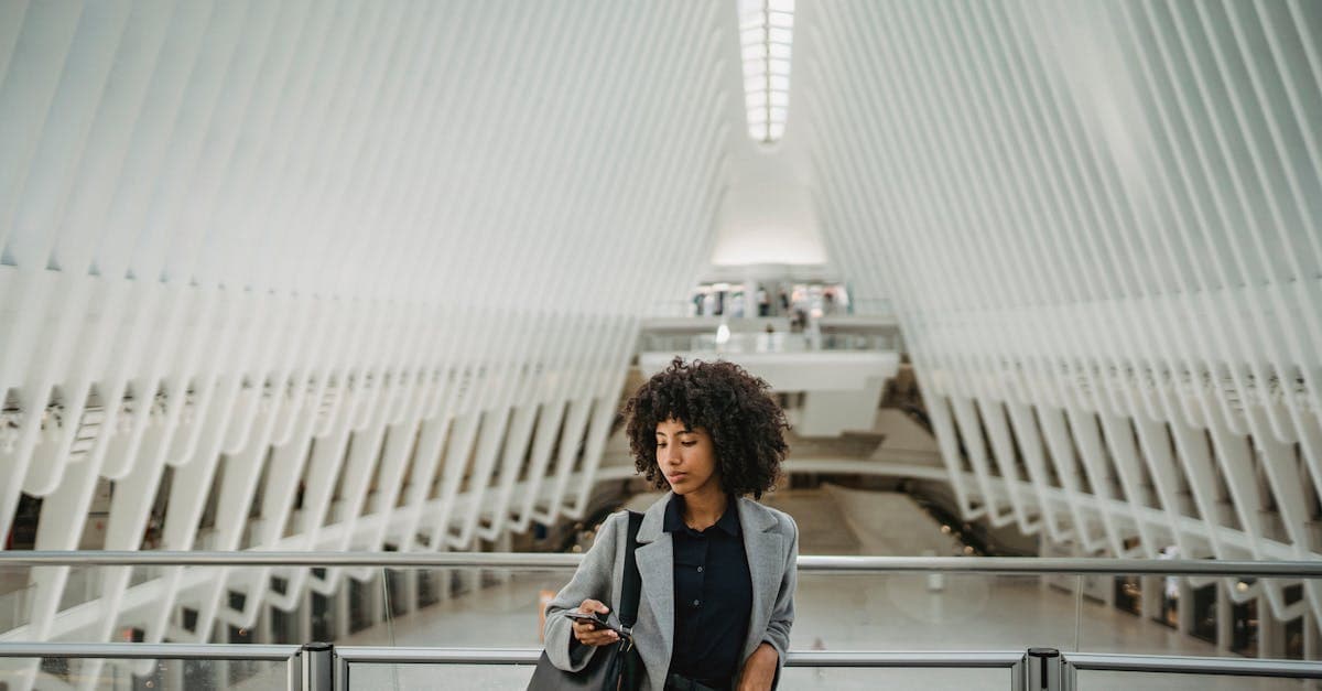 A fashionable woman with curly hair using a smartphone in a modern architectural setting.