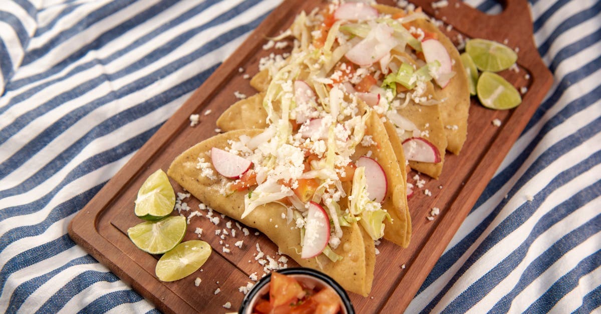 Tacos mexicanos servidos en tabla de madera con limones frescos y aderezos para platillos principales del mediodía.