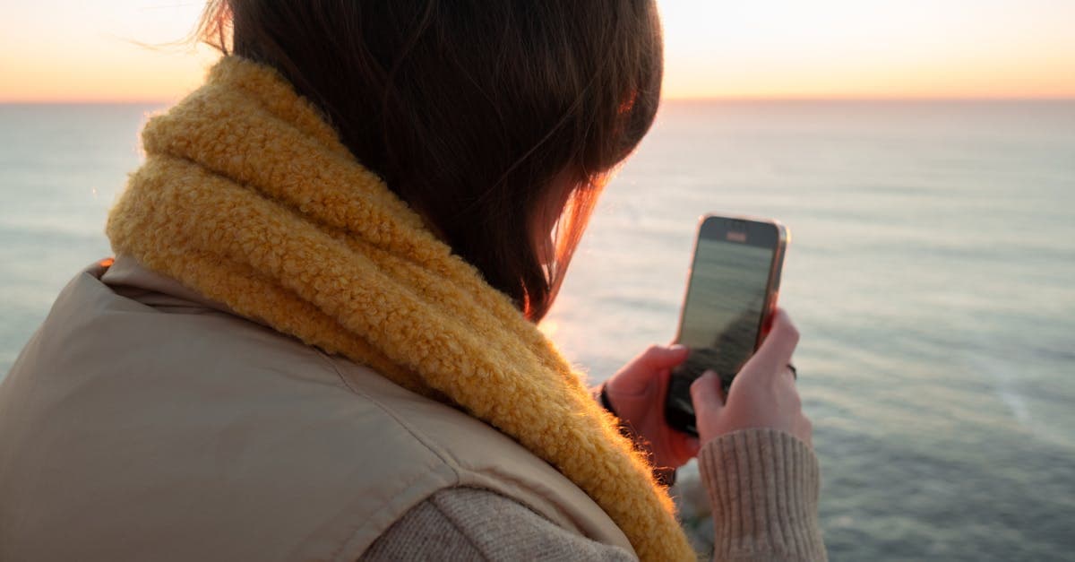 Woman photographing ocean sunset on smartphone, staying connected with a travel eSIM after a Sydney to Singapore flight.