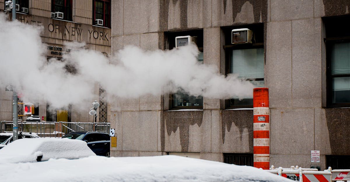 Steam rising from a street vent on a snow-covered New York City block in winter.