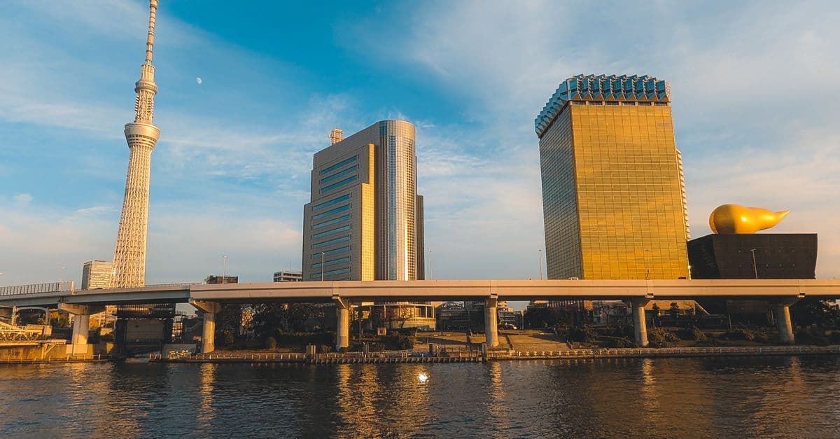 Tokyo Skytree and the Asahi Beer Tower reflected in the river during daylight hours.