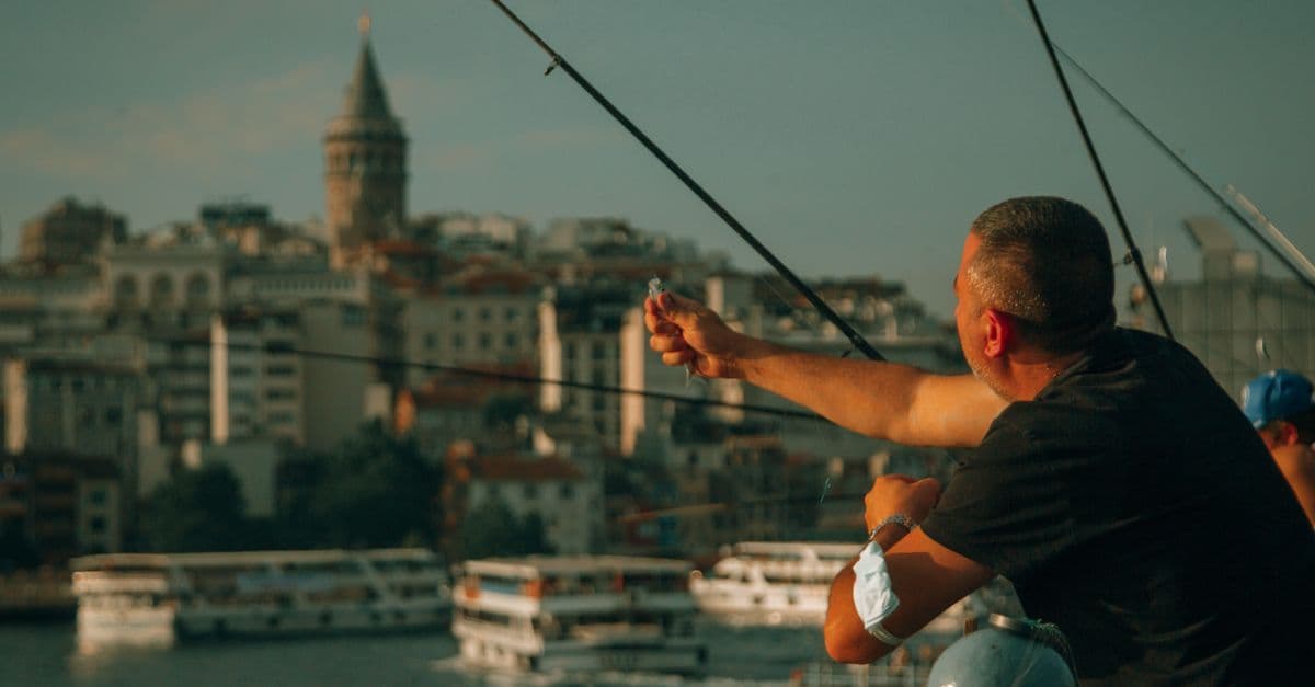 Ein Mann angelt auf der Galatabrücke in Istanbul, im Hintergrund der Galataturm und Fähren.