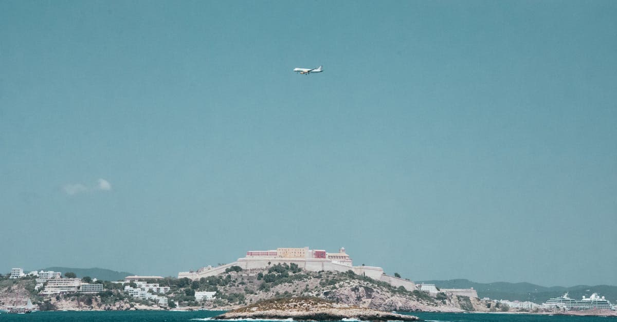 Aircraft flies low over Ibiza's Mediterranean coastline, illustrating the direct flights to Ibiza available from UK airports