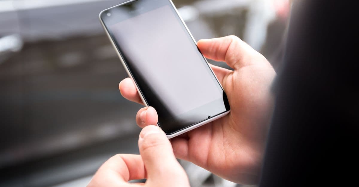 屋外でスマートフォンを両手で持ち、dアカウントのIDとパスワードの基本構造を確認している場面