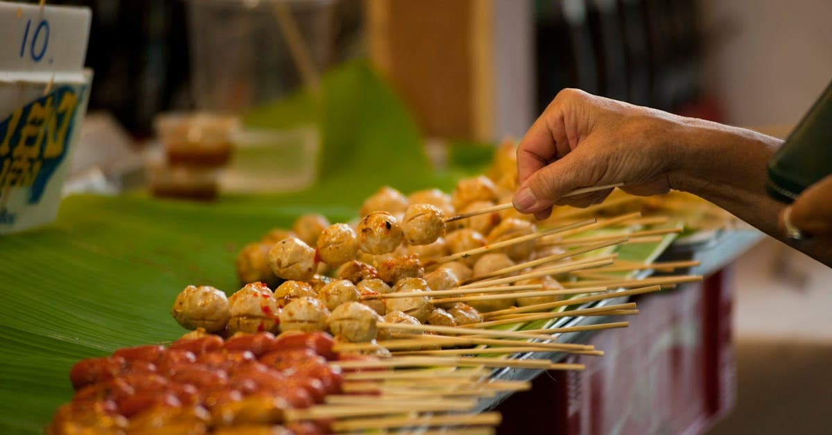 Hand wählt Spieße an einem belebten Bangkok Streetfood-Stand im bekanntesten Viertel der Stadt
