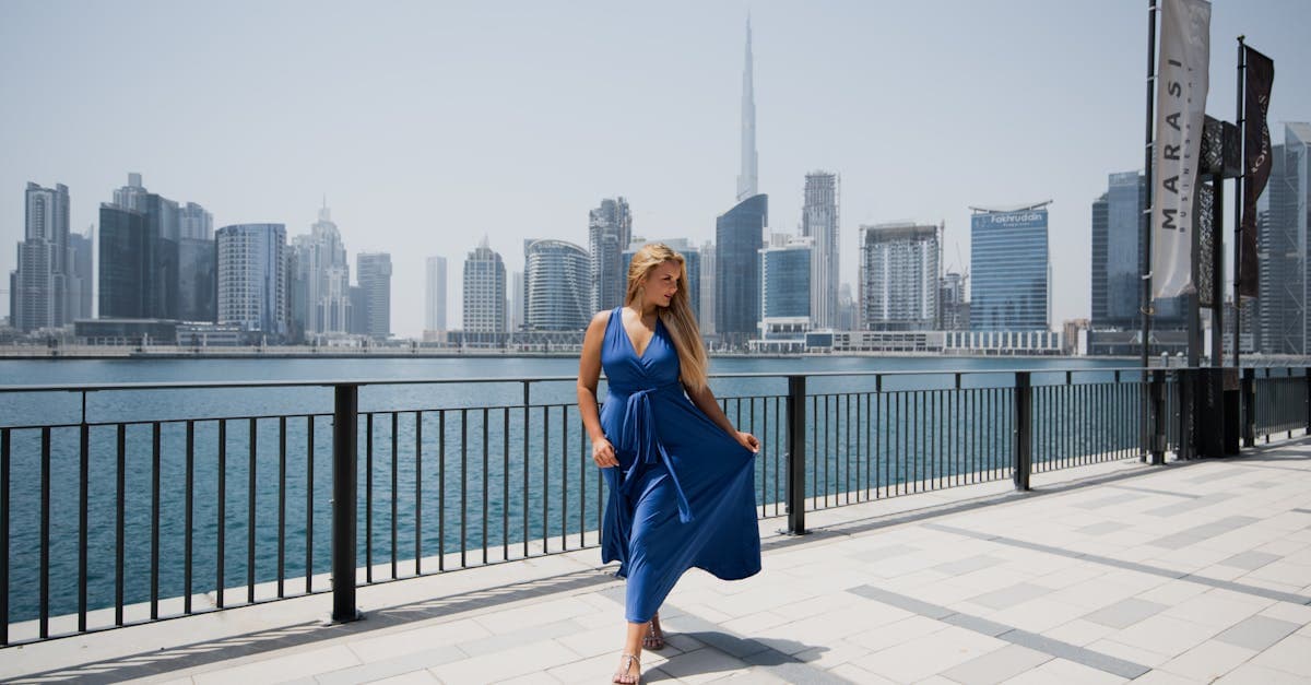 Donna con abito blu elegante posa davanti allo skyline di Dubai in una giornata soleggiata