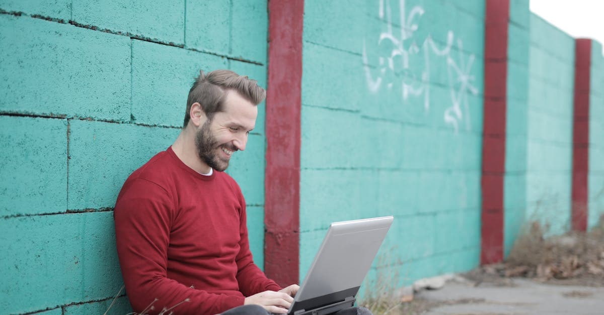 Hombre con suéter rojo usando portátil en pared de graffiti, representando estilo de vida remoto con wifi portátil.