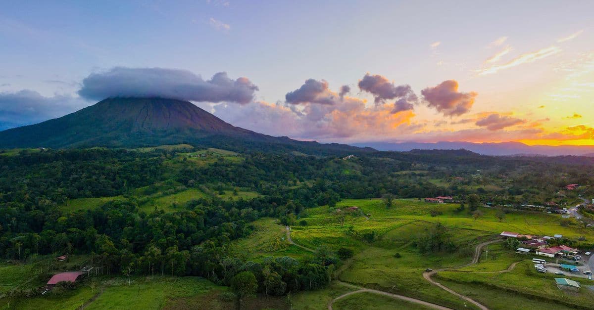 A cloud-draped volcano rises above Costa Rica’s green countryside at sunset.