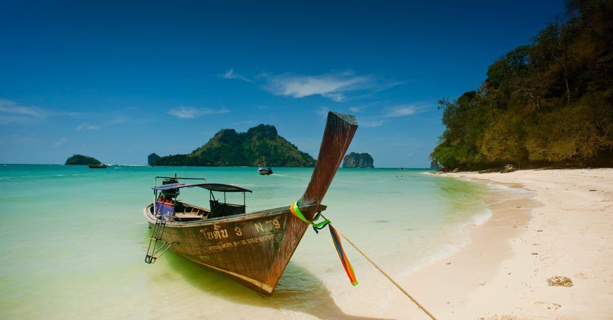 Longtail boat moored on Krabi's turquoise Ao Nang beach, achievable on a budget thailand holiday.