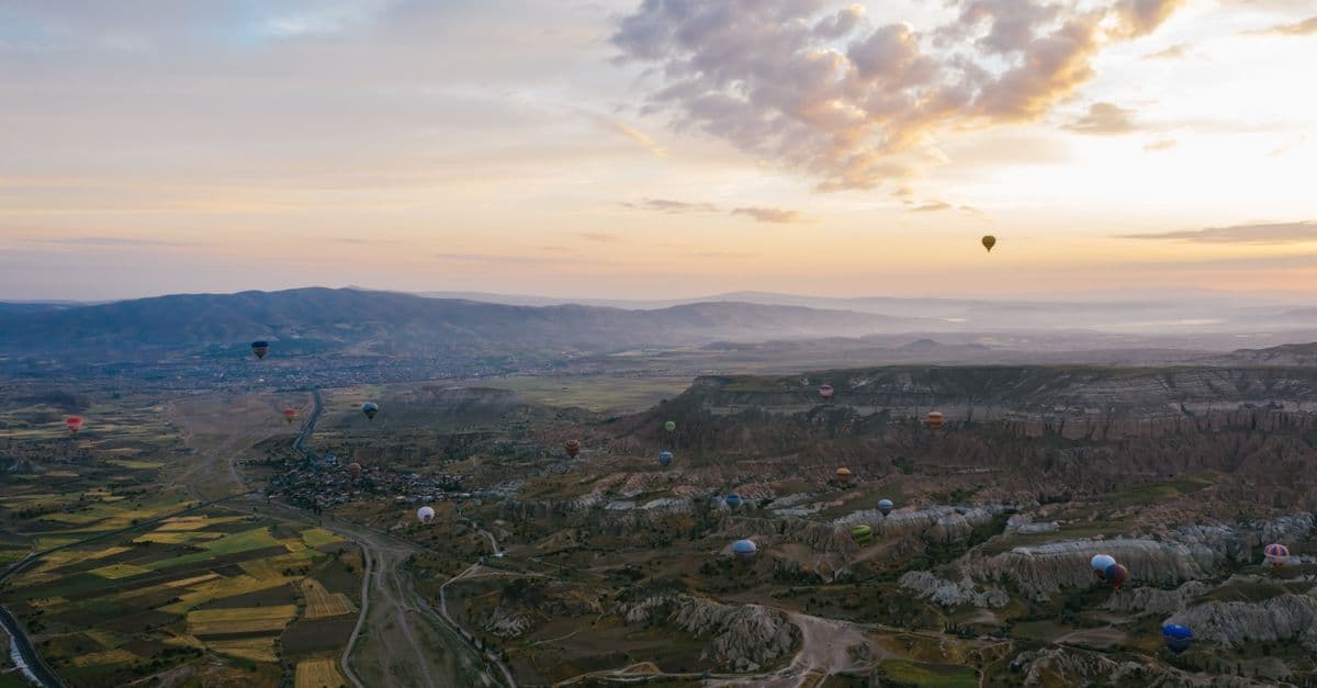 Heißluftballons schweben bei Sonnenaufgang über der weiten Landschaft Kappadokiens.