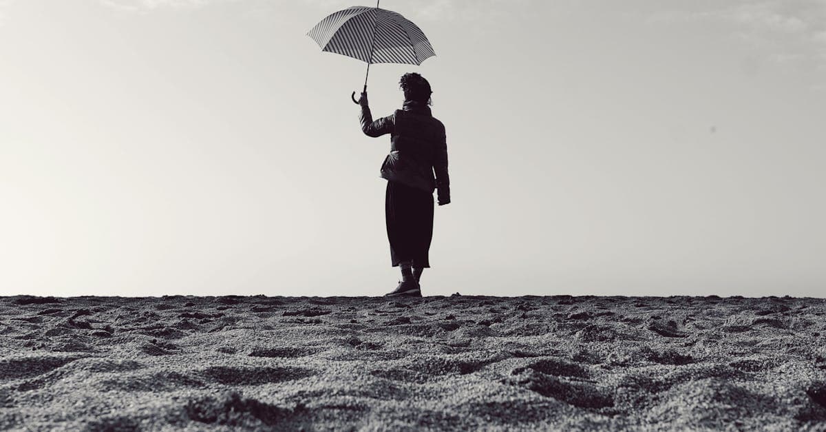 砂浜に佇み傘を持つ女性のシルエット、一人旅 海外を安全に楽しむ女性旅行者のイメージ