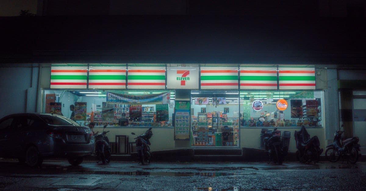 Tienda 7-Eleven iluminada de noche con vehículos estacionados, donde puedes comprar tarjetas de regalo Google Play