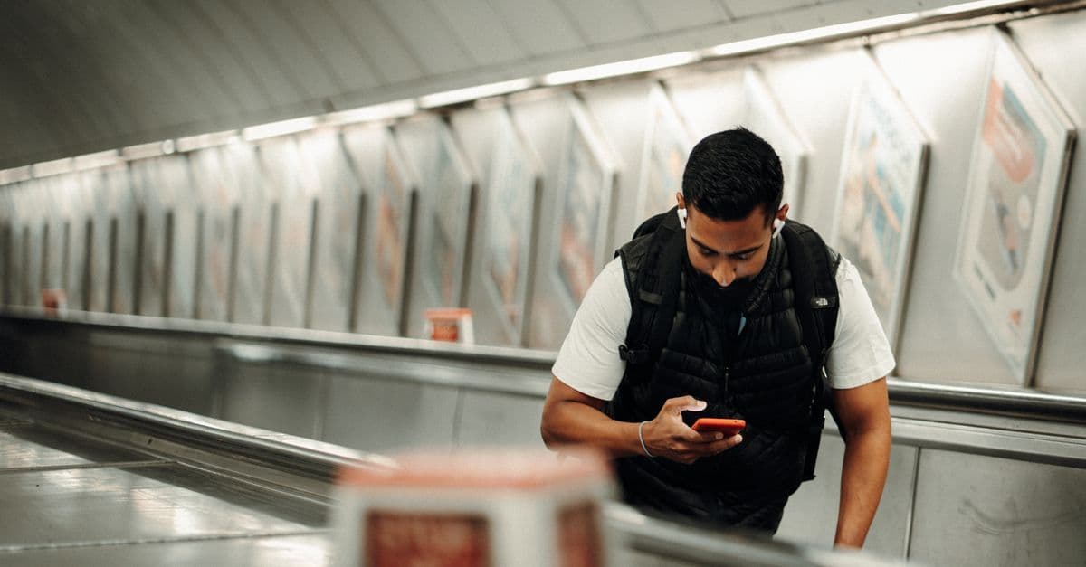 Young man using a smartphone to manage his eSIM data plan on a London Underground escalator.