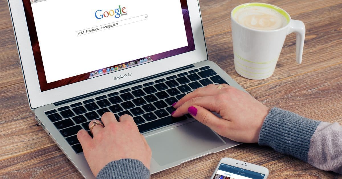 Hände tippen auf einem MacBook Air mit geöffneter flüge google Suche und einer Kaffeetasse daneben.