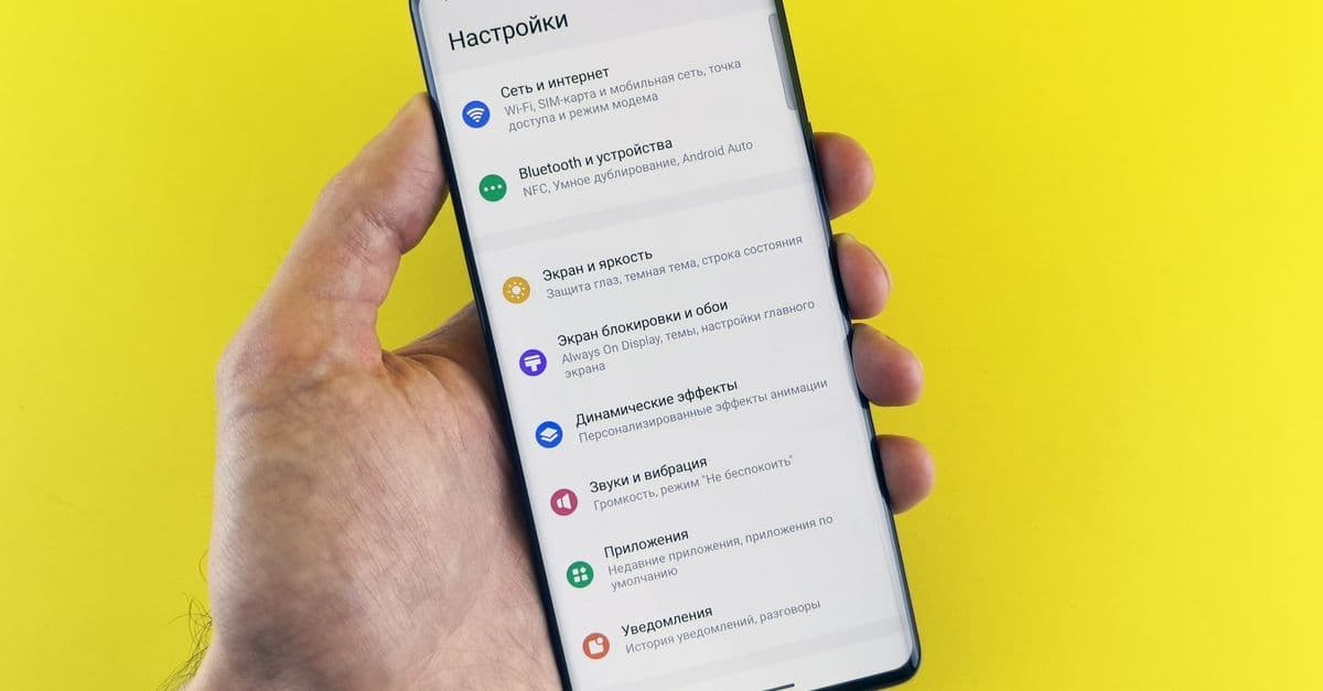 Mão segurando smartphone com menu de configurações aberto em fundo amarelo para configurar eSIM