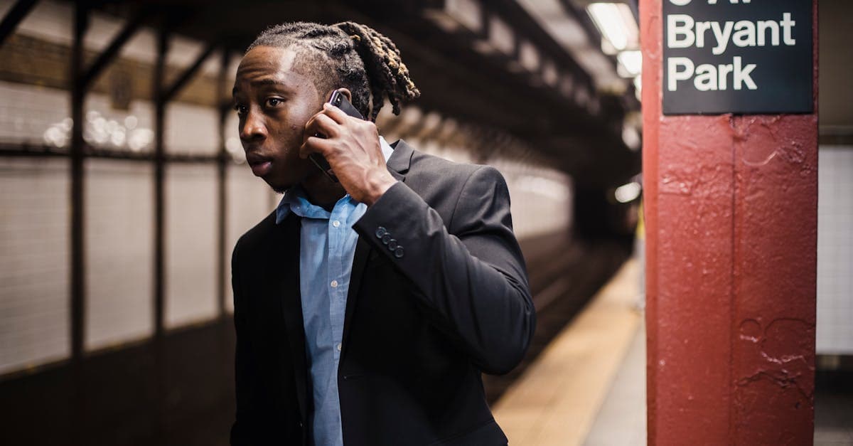 Man in formal wear talking on a blackberry phone while waiting anxiously at a New York subway station.