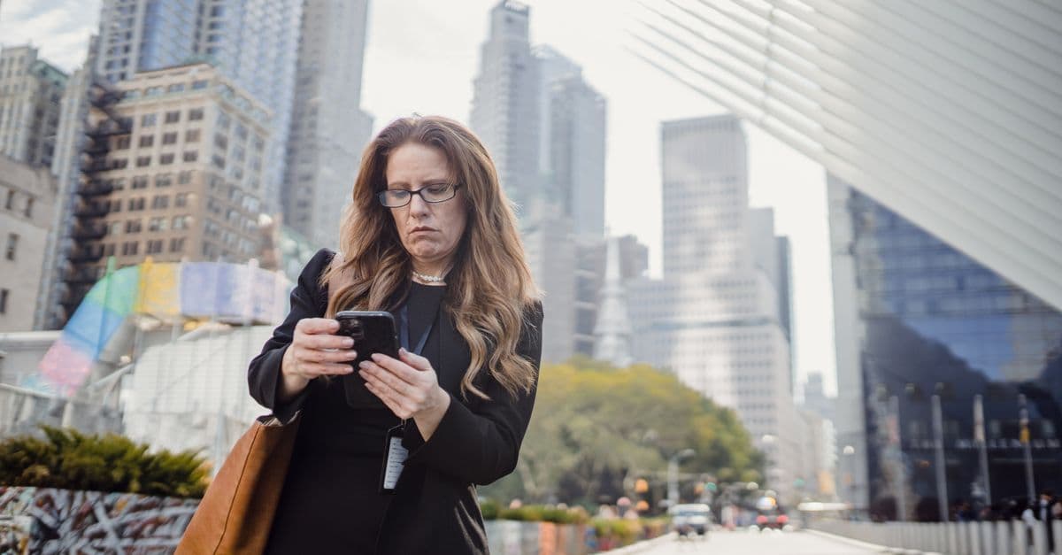 Businesswoman troubleshooting siri not working on her iPhone while walking through a modern city street.