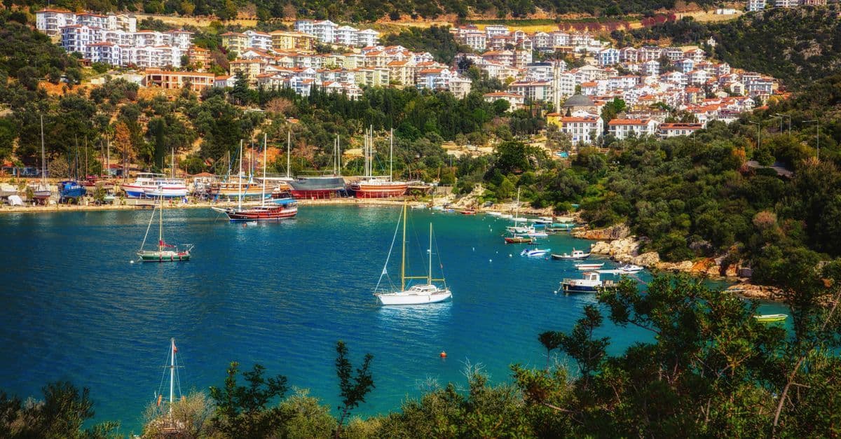 Segelboote liegen in der türkisblauen Bucht von Kaş, am Hang darüber stehen weiße Häuser.
