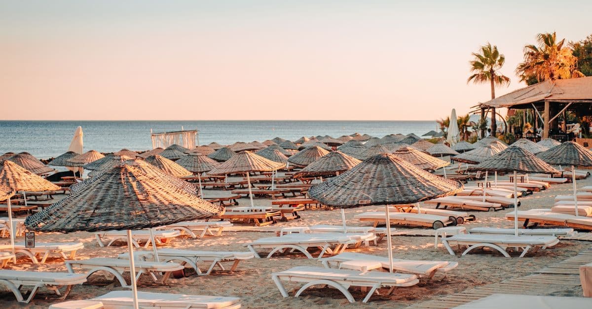 Ruhiger Strand mit leeren Sonnenliegen und Strohschirmen am Meer – ideal für die beste Reisezeit im Türkei Urlaub.